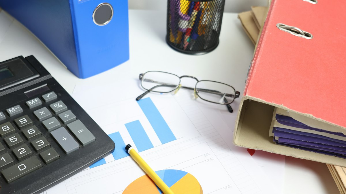 Bureau avec calculatrice, classeurs, lunettes et graphiques financiers imprimés