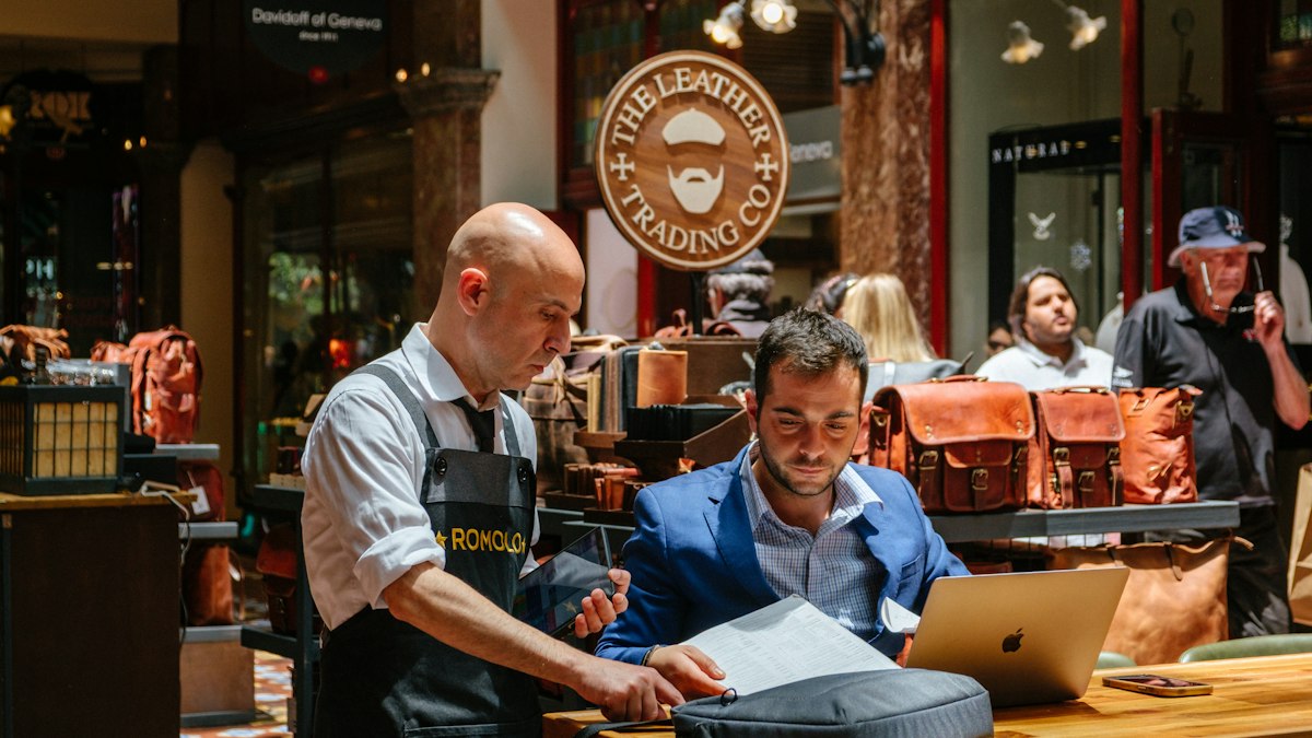 Un commerçant en tablier et un repreneur examinent des documents dans une boutique de maroquinerie