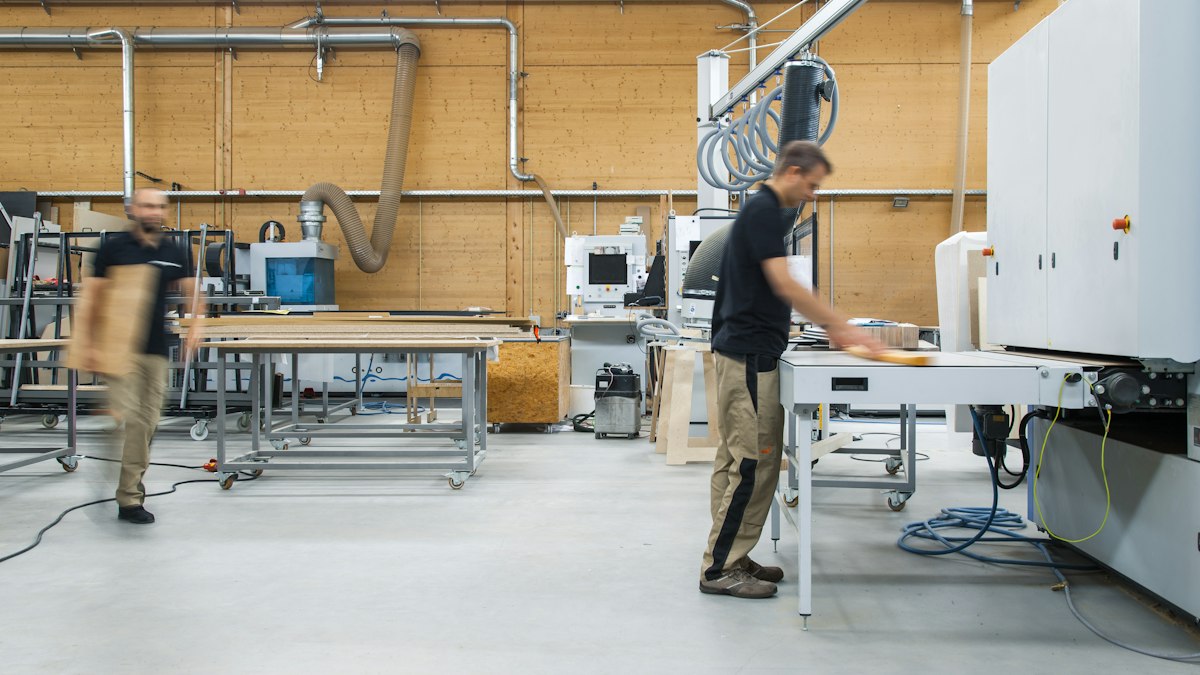 Atelier de menuiserie d'une PME : un salarié travaille sur une machine pendant qu'un collègue traverse l'atelier